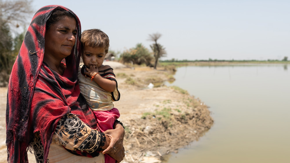 Mor og datter ved siden av stillestående flomvann i Pakistan