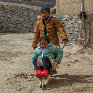 Et søskenpar på 6 og 7 år i Afghanistan leker ute med sine nye vinterjakker fra UNICEF.