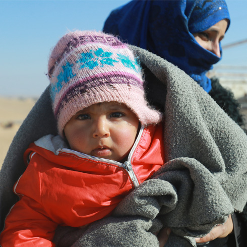 En liten jente med pledd rundt seg i Syria