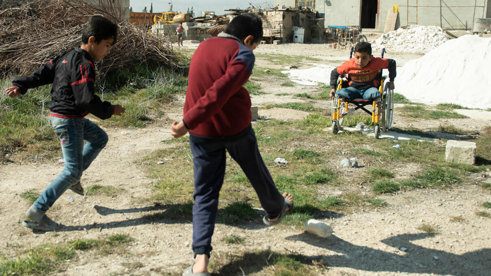 To barn bruker en plastflaske som fotball og skyter mot en gutt i rullestol som er målvakt, Syria