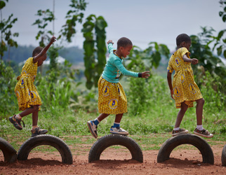 Tre barn balanserer på bildekk satt opp i sanden, Ghana