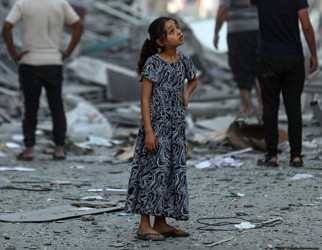 En jente står og ser på ruiner rundt seg, Gaza