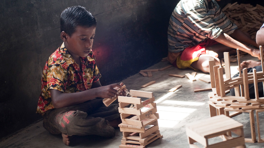 En gutt bygger tårn av kapla, Bangladesh