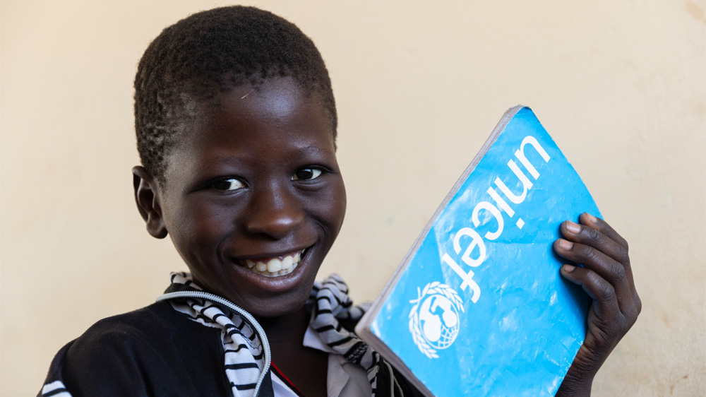 En elev viser frem skriveboken sin fra UNICEF, Gambia