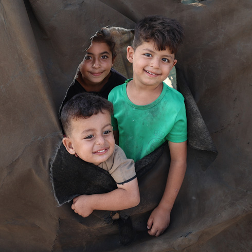 Tre barn titter ut gjennom et hull i en teltduk, Gaza