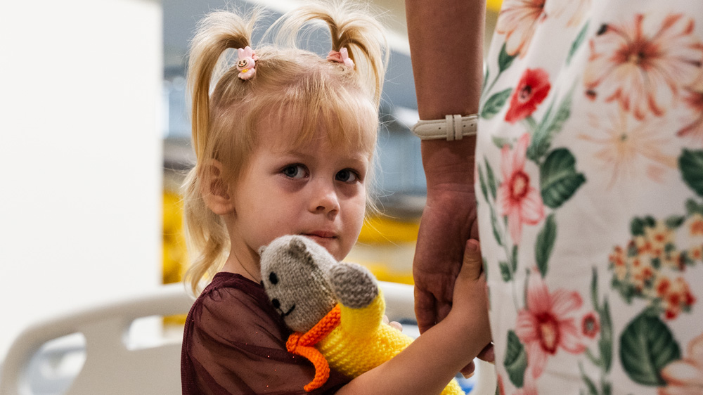 Ei jente holder mamma i handa og klemmer bamsen sin inne på et sykehus, Ukraina