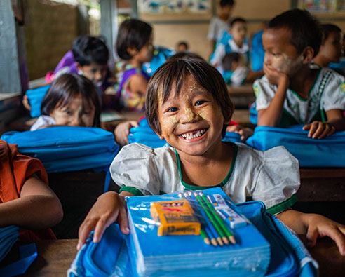 San smiler til kamera i Myanmar med skolesaker fra UNICEF – fylt med det hun trenger for å lære.