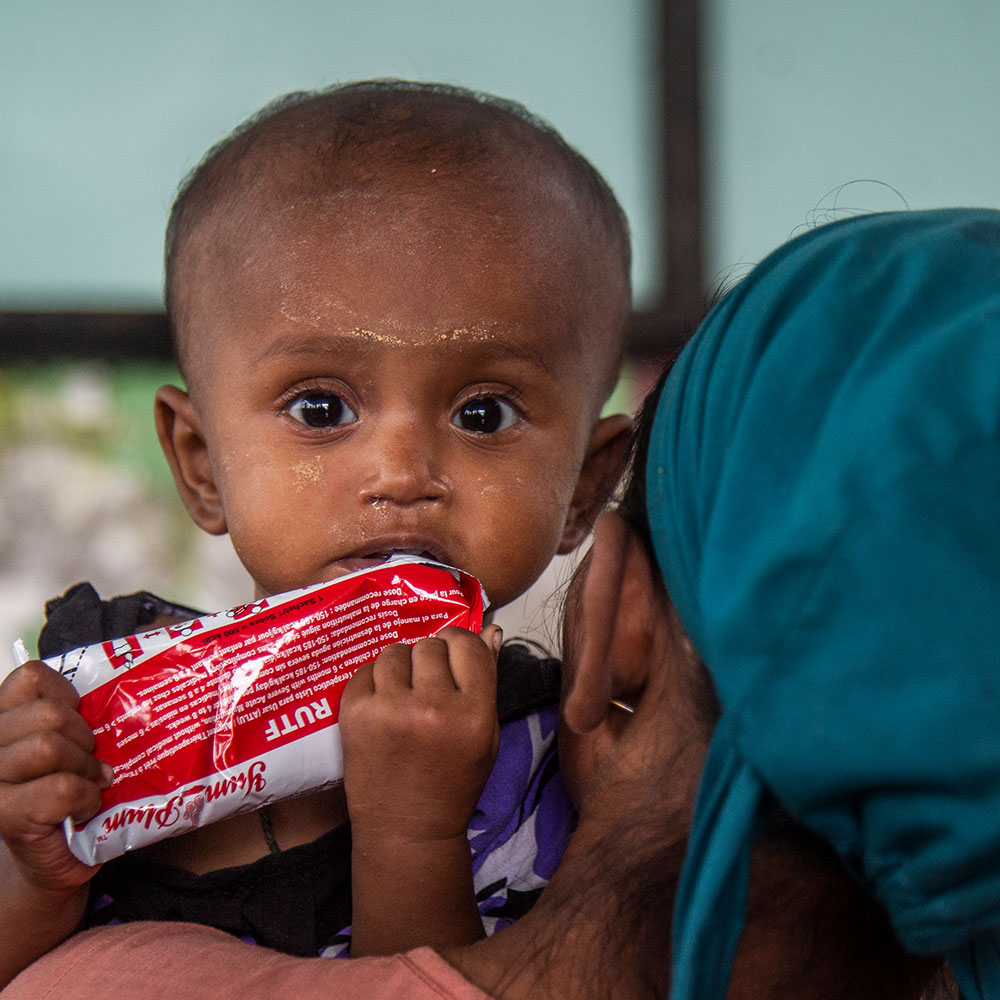 Et barn i Myanmar holdes av moren sin og får nødmat