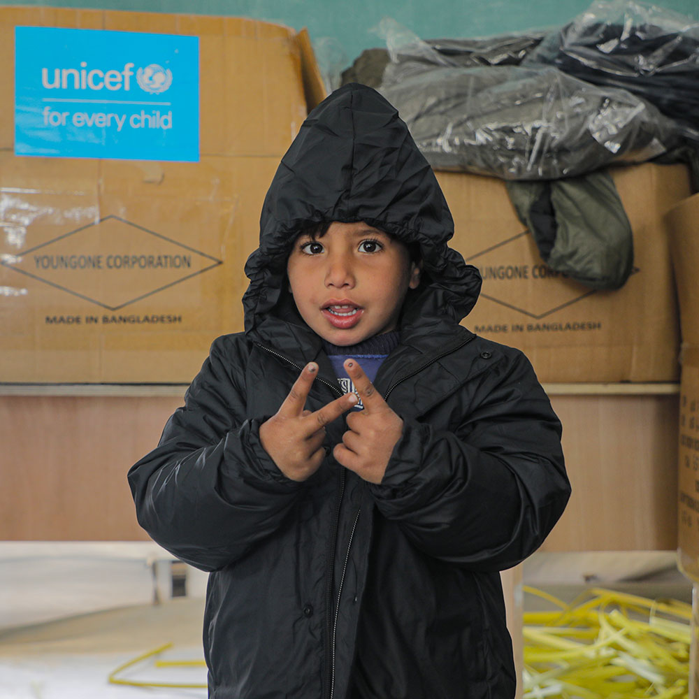 En gutt har fått varme klær av UNICEF, han har på seg en svart, tykk jakke