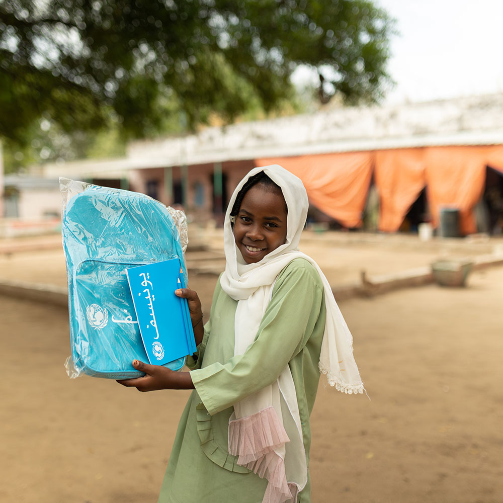 Et barn holder opp en skolesekk fra UNICEF.