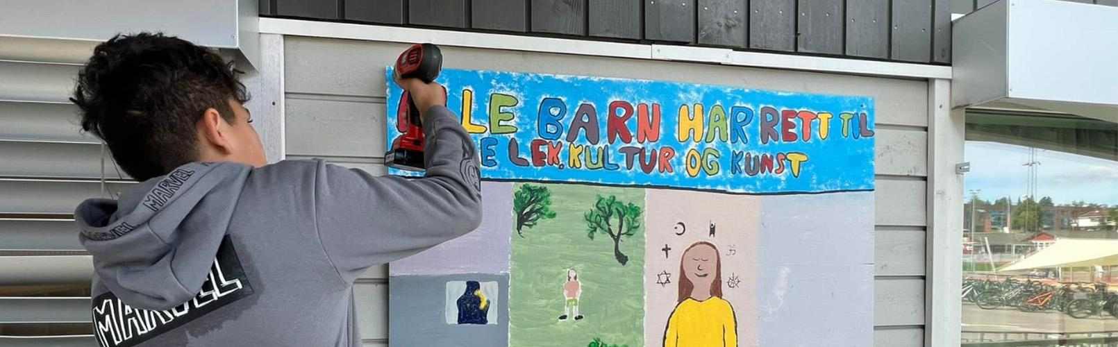 Gutt henger opp plakat med "rett til lek"