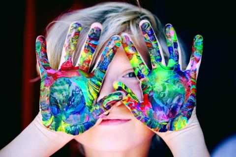 Bilde av barn med fargelagte hender foran ansiktet.