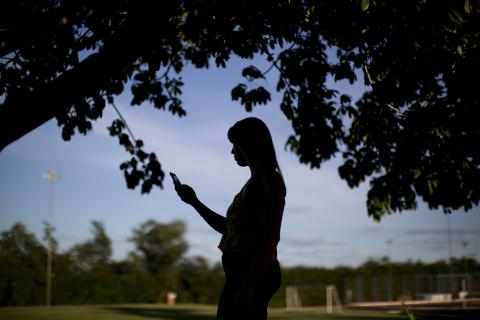En anonymisert jente står under et tre mens hun studerer telefonen sin.