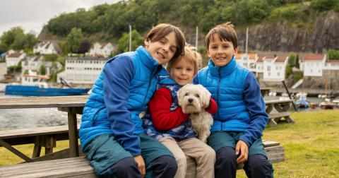 Tre barn sitter på en benk sammen med en hund