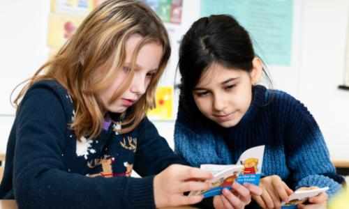 To jenter ser i bok på skolen