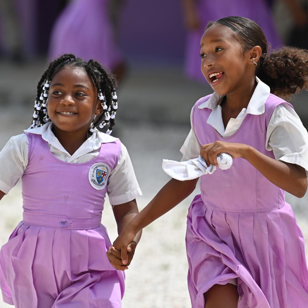 To jenter i lilla skoleuniform løper hånd i hånd, Belize