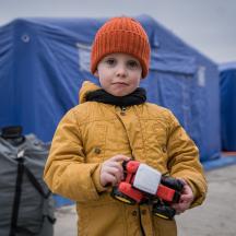 Vinterkledd ukrainsk barn med leketraktor foran telt